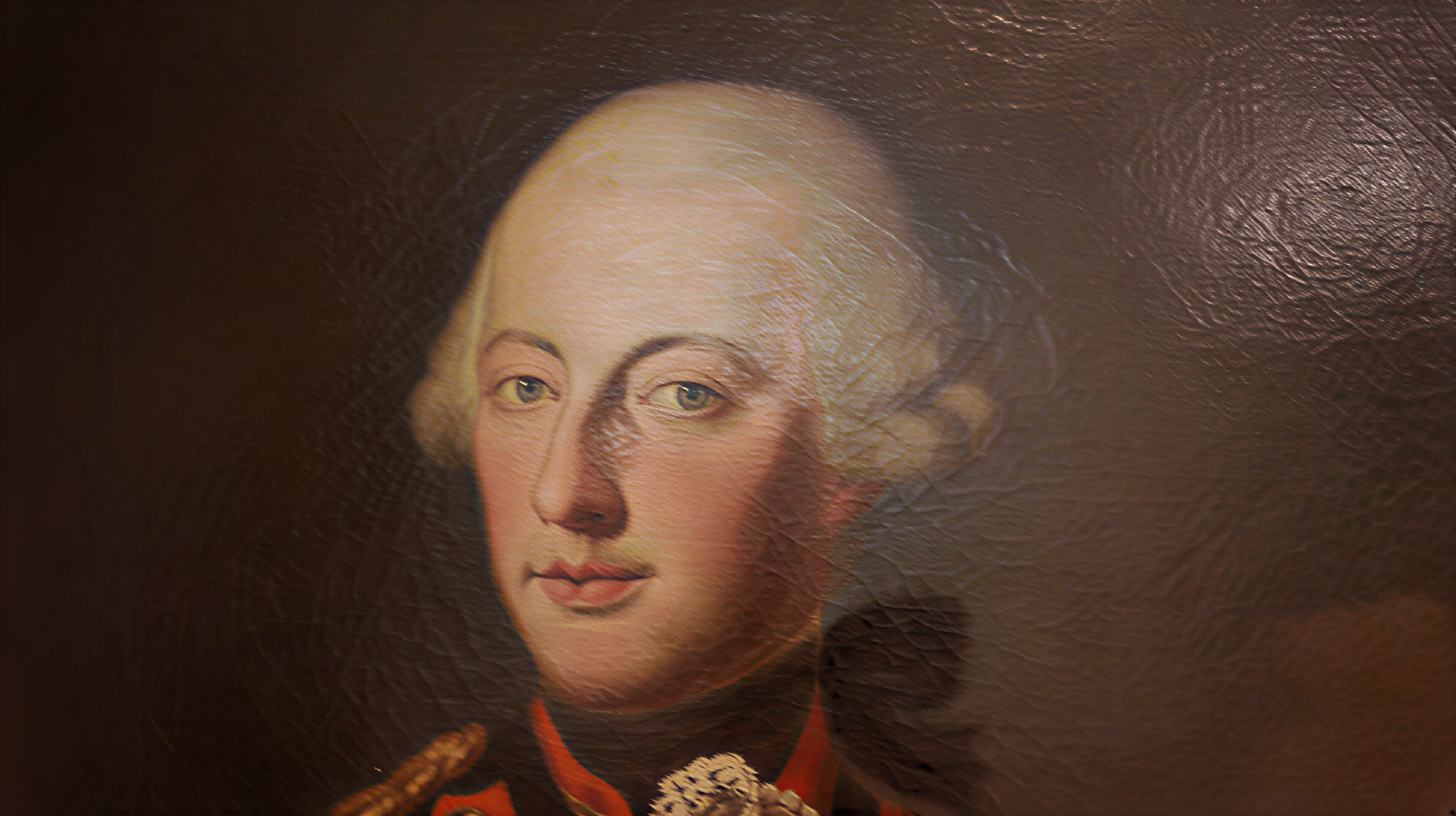 Détail d’un portrait peint montrant un homme aux cheveux clairs, vêtu de rouge.