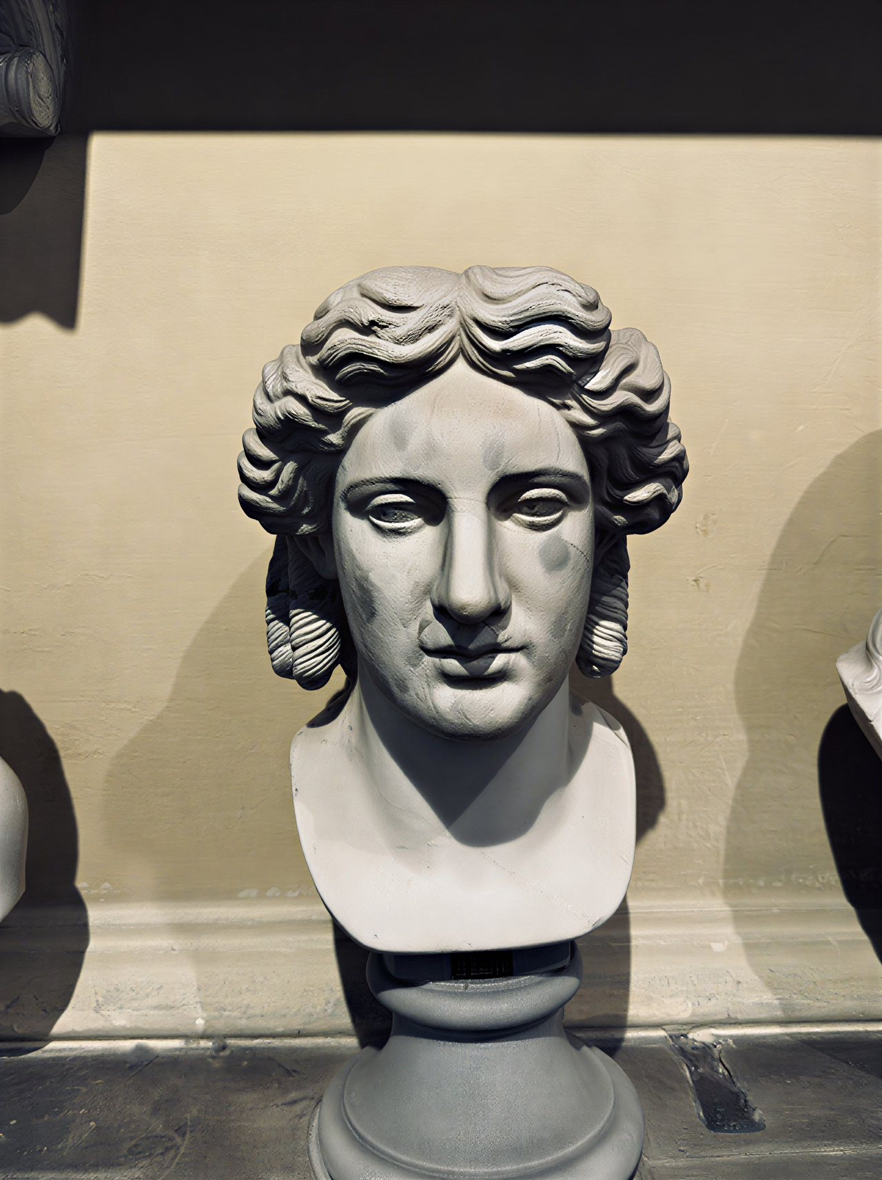 Sculpture antique représentant un visage masculin avec des cheveux ondulés, exposée dans les Musées du Vatican, symbolisant l'idéal de beauté classique.
